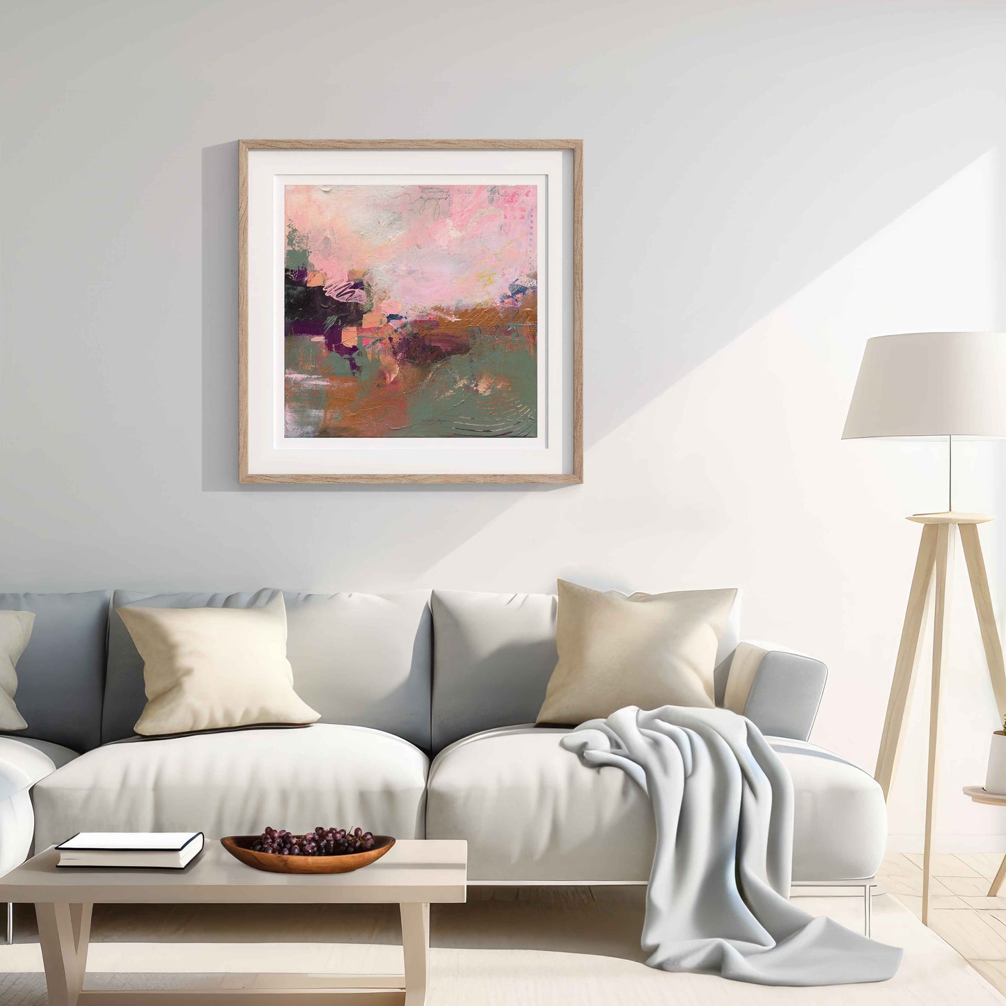 Living room with a gray sofa, framed abstract pink and green artwork, and a lamp.